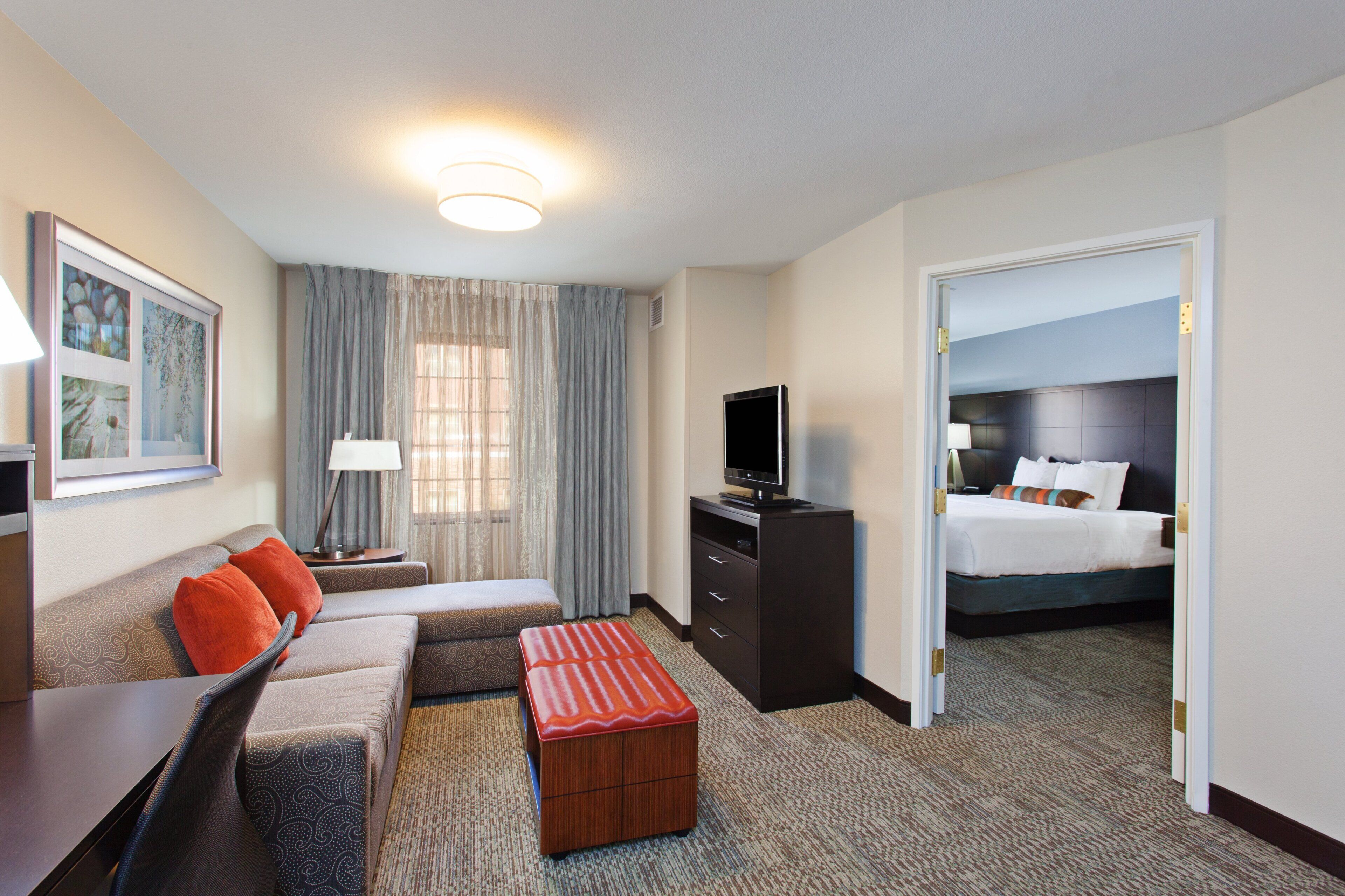 Ein Hotelzimmer mit Sofa, Fernseher, Schreibtisch, Lampe, Kommode und einem Bett.
