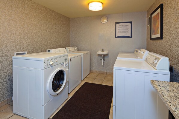 A laundry room with two front-loading washing machines, a sink, and a notice board. - Staybridge Suites Fairfield Napa Valley Area by IHG (Fairfield)