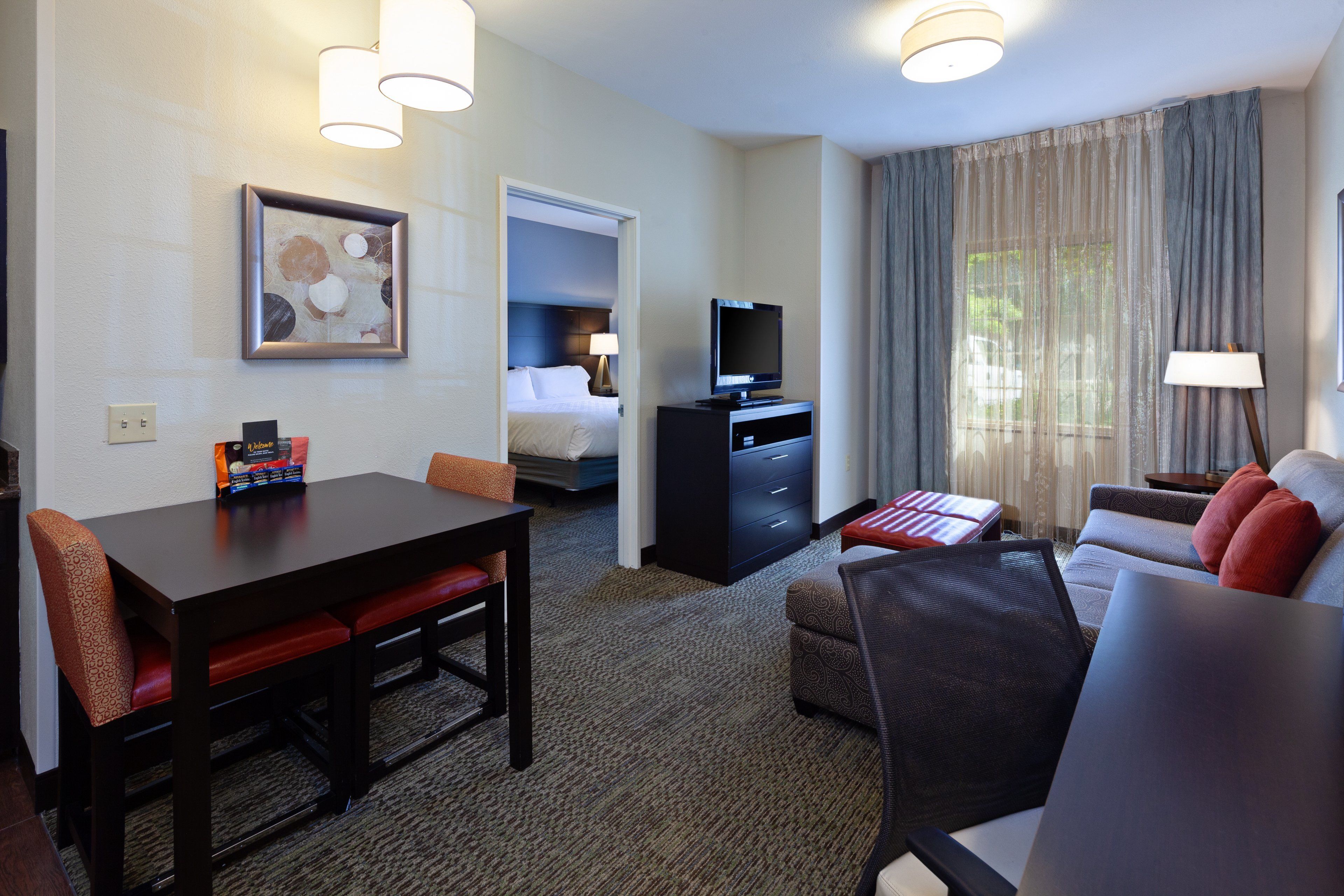 Una habitación de hotel con una mesa de comedor, un sofá, un televisor y una cama.