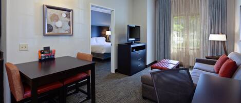 Una habitación de hotel con una mesa de comedor, un sofá, un televisor y una cama.