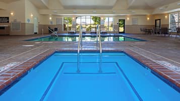 Una gran piscina interior con agua cristalina y azul, rodeada de sillones de descanso y una zona cubierta con asientos.