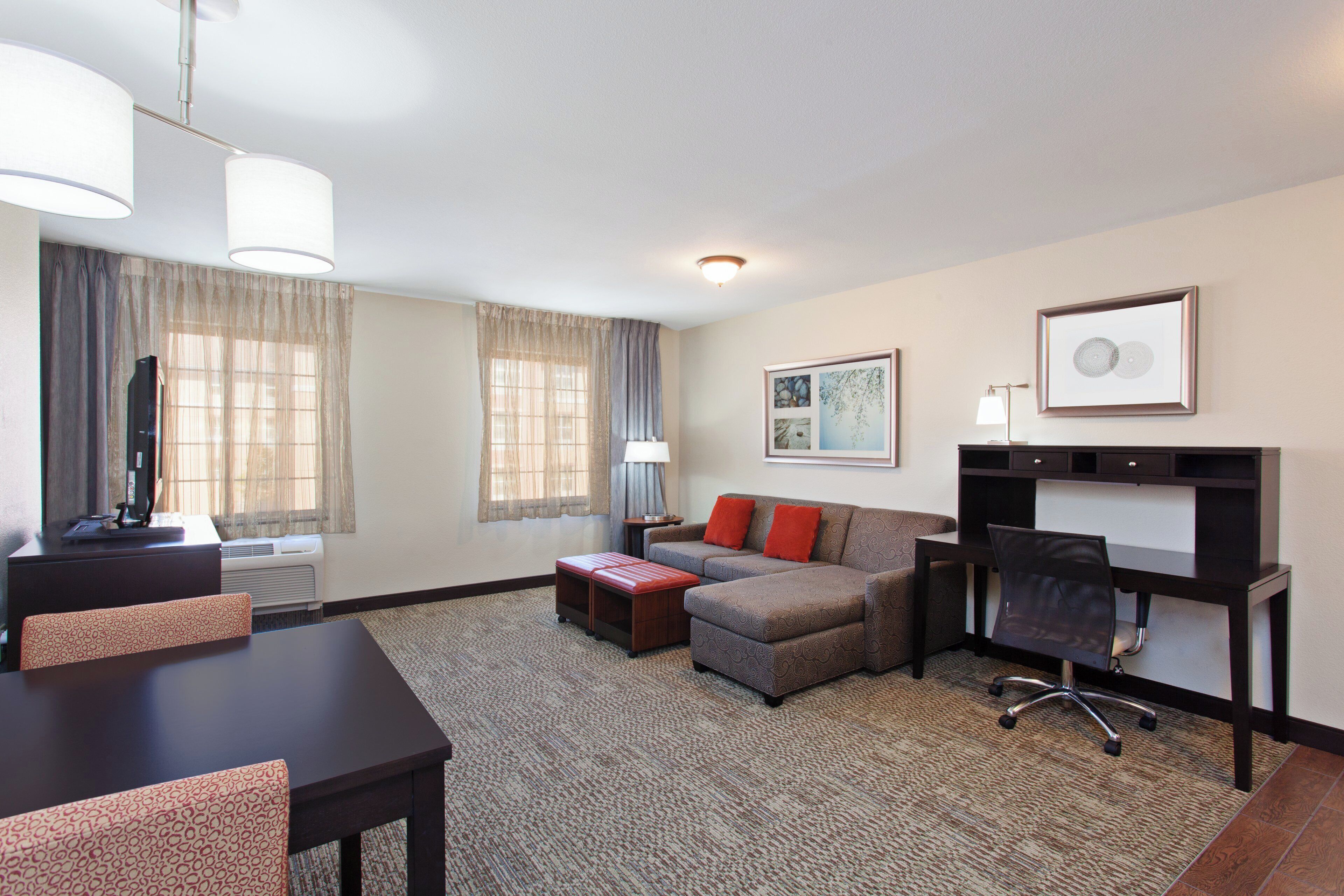 A hotel room with a sofa, a desk, a chair, a television, and a framed picture on the wall.