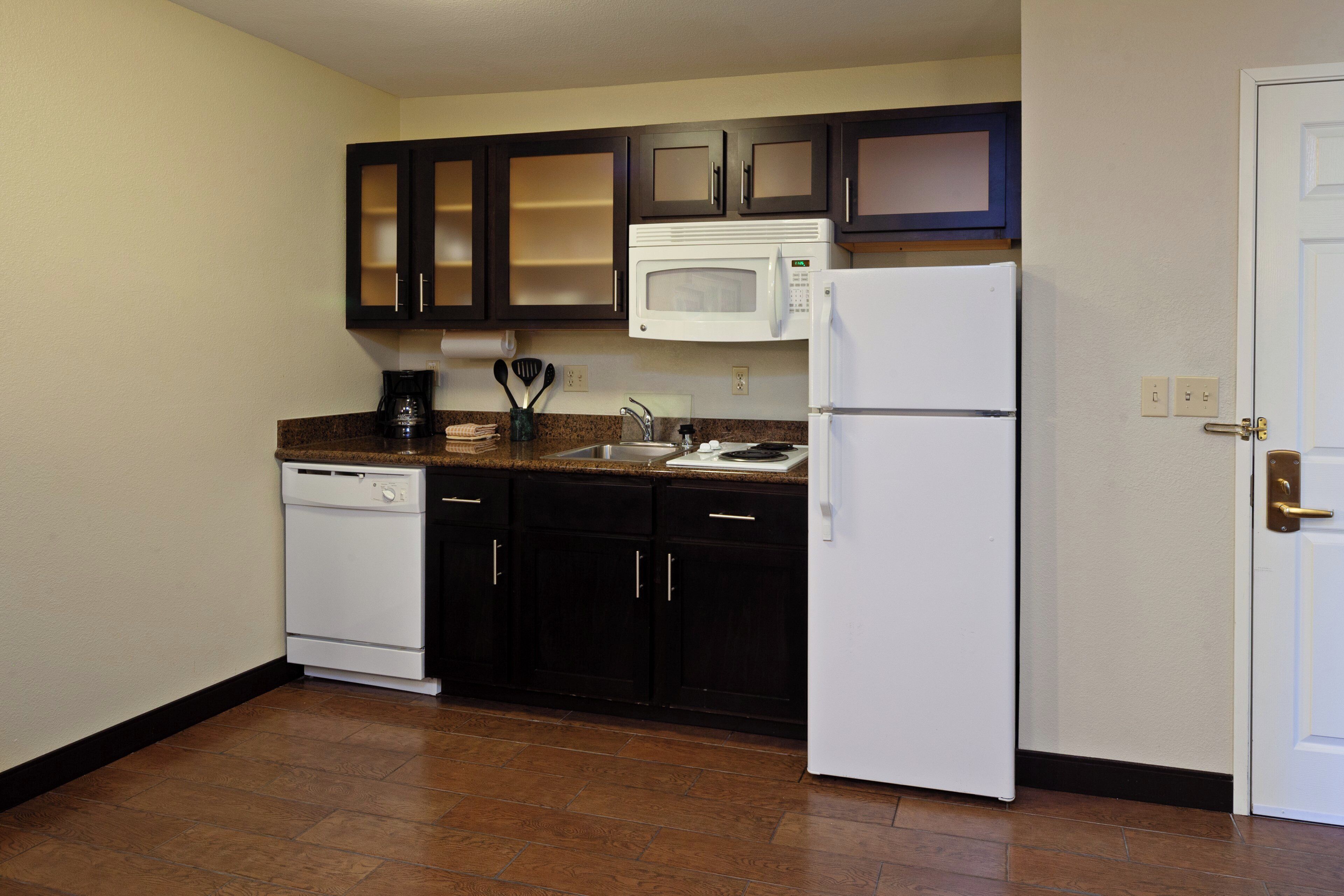 A compact kitchen with dark cabinets, a white microwave, a white refrigerator, and a dishwasher.