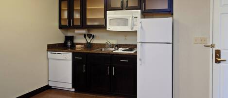 A compact kitchen with dark cabinets, a white microwave, a white refrigerator, and a dishwasher.