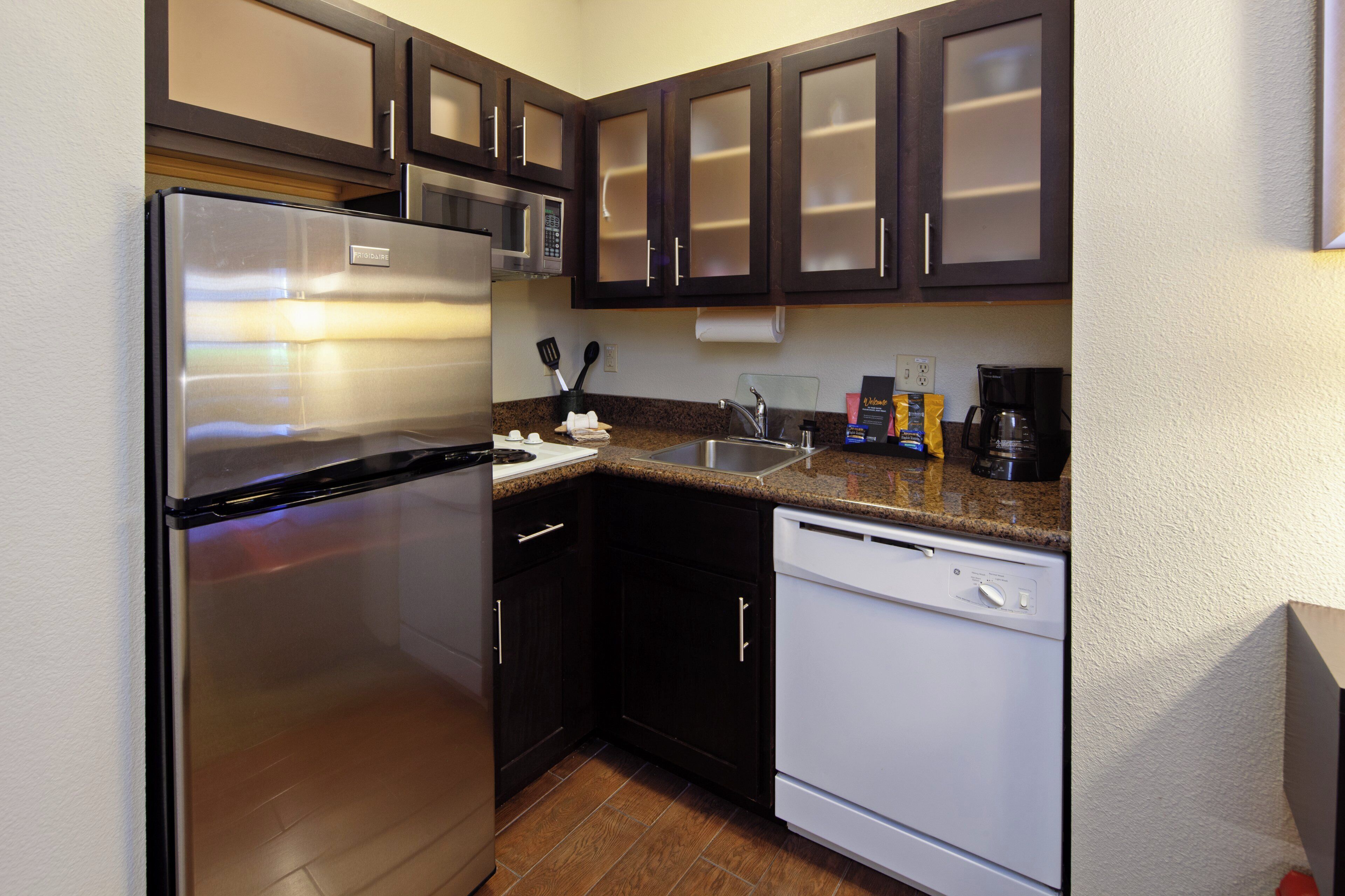 A compact kitchen with a stainless steel refrigerator, a microwave, a coffee maker, and a dishwasher.