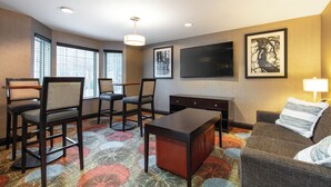 A hotel room with a seating area, a flat-screen TV, a large window, and a patterned carpet. - Staybridge Suites Fairfield Napa Valley Area by IHG (Fairfield)