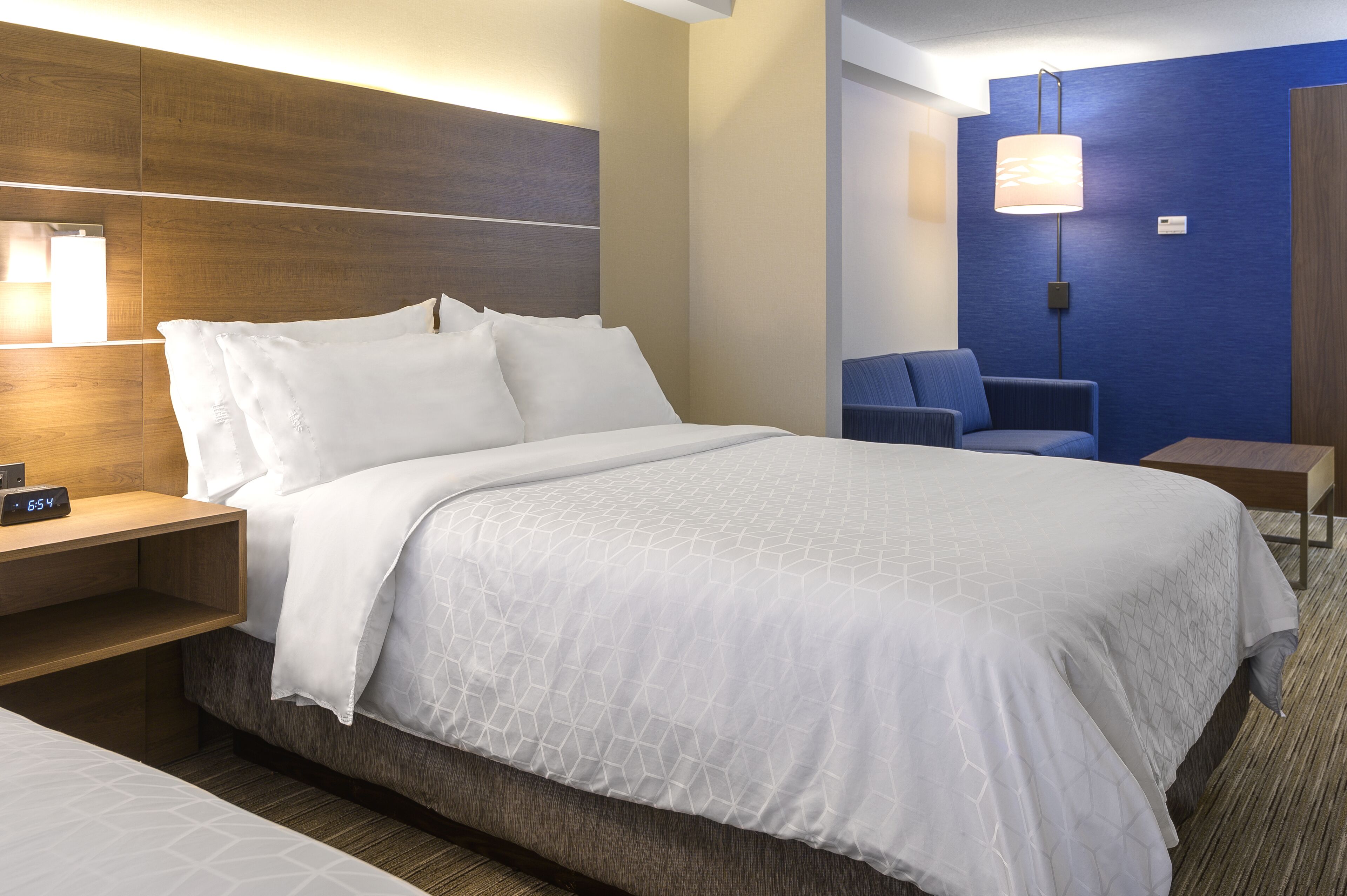 A hotel room with a large bed, a bedside table with a lamp, a chair, and a small table.