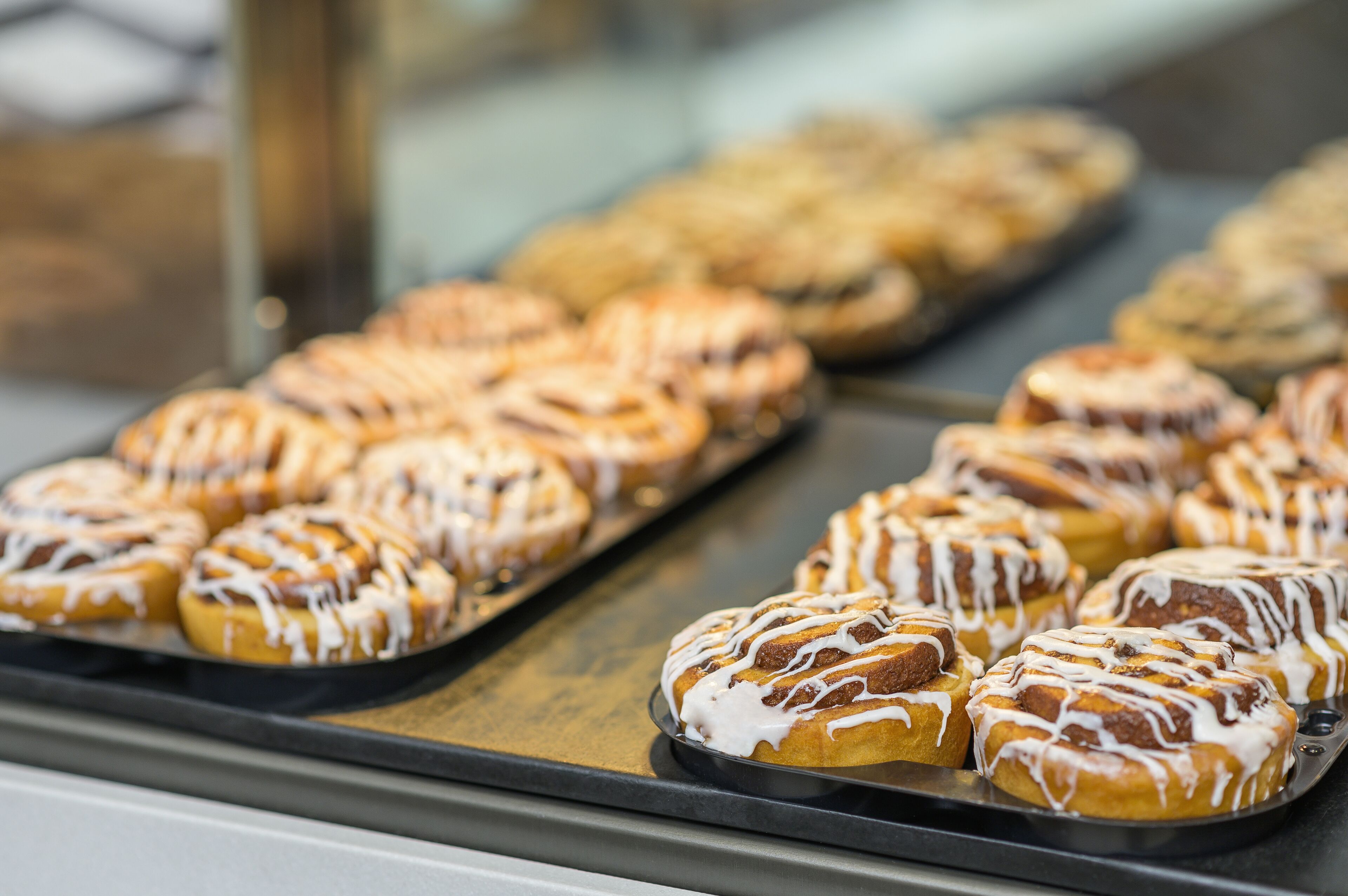 A display of cinnamon rolls with white icing in a bakery.