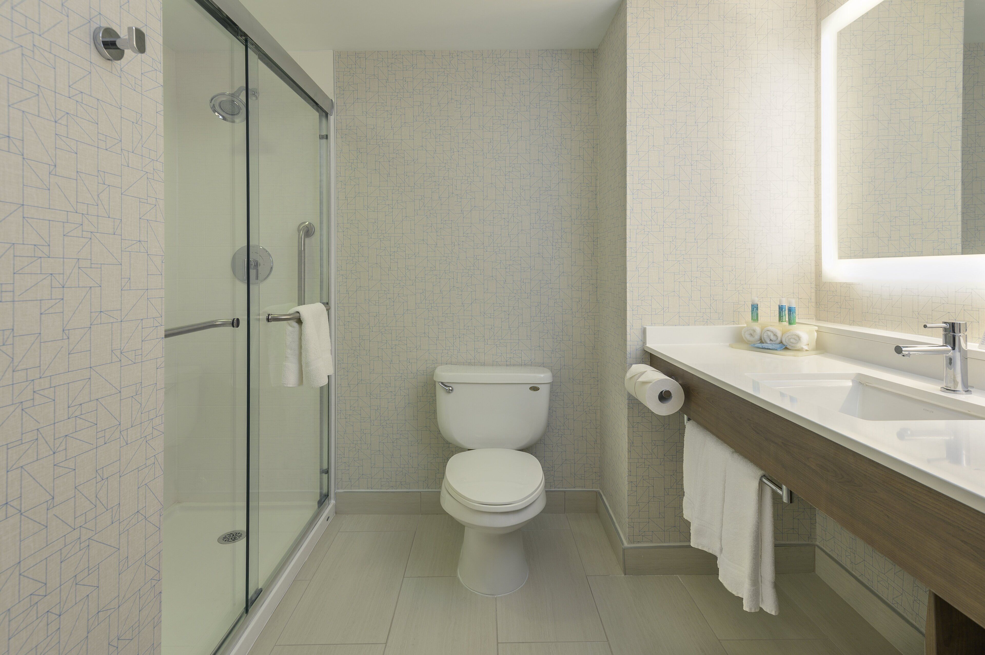 Un baño moderno con cabina de ducha de vidrio, inodoro y tocador con espejo.