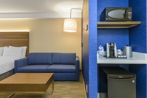 A hotel room with a bed, a blue sofa, a wooden coffee table, a microwave, a coffee machine, and a mini fridge. - Holiday Inn Express & Suites North Bay by IHG (North Bay)