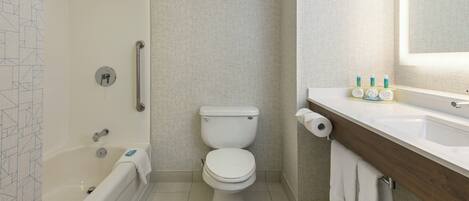 A bathroom with a bathtub, toilet, and a vanity with toiletries.