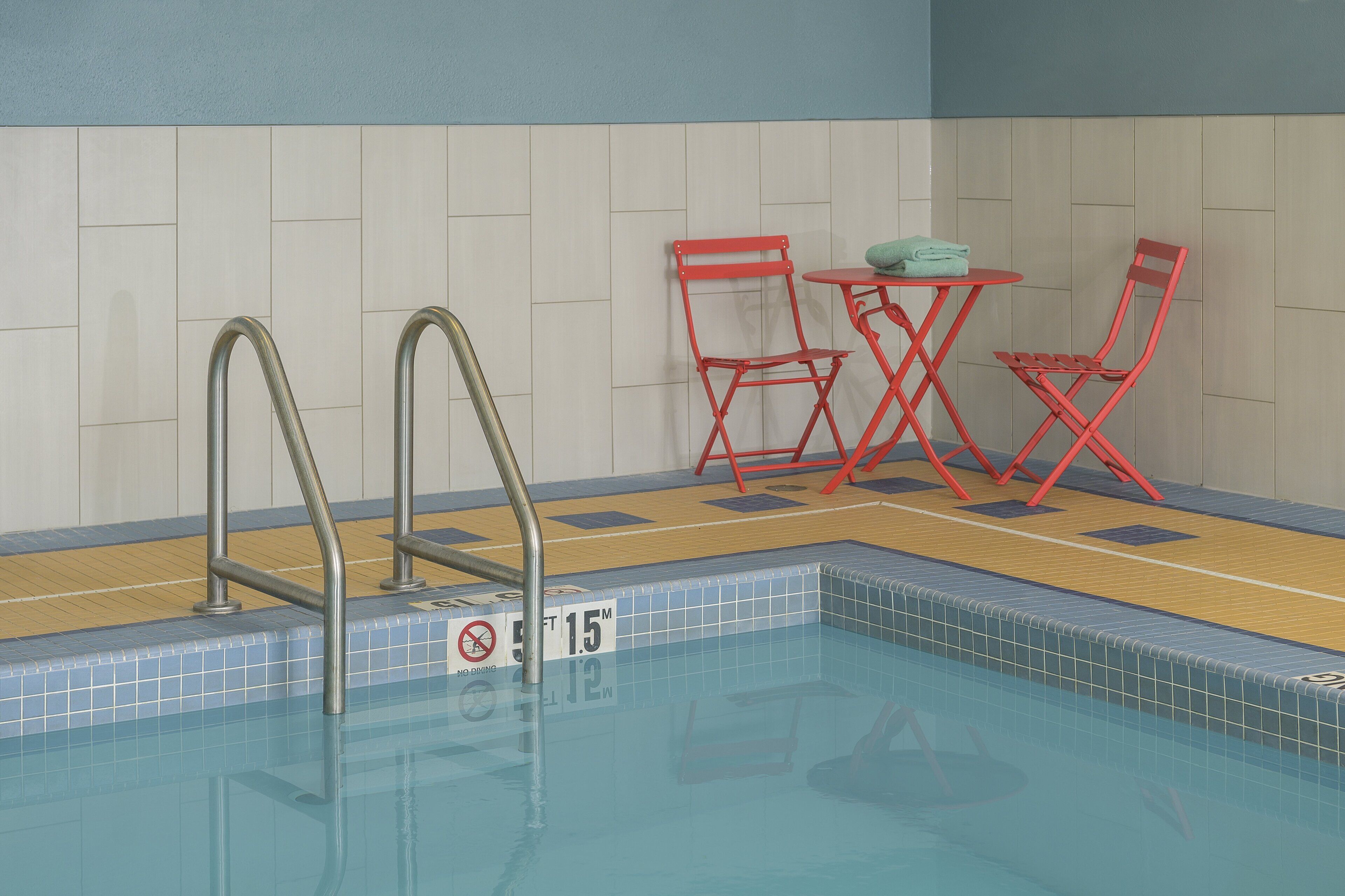 En swimmingpool med metalstiger, røde klapstole og et bord med et håndklæde.