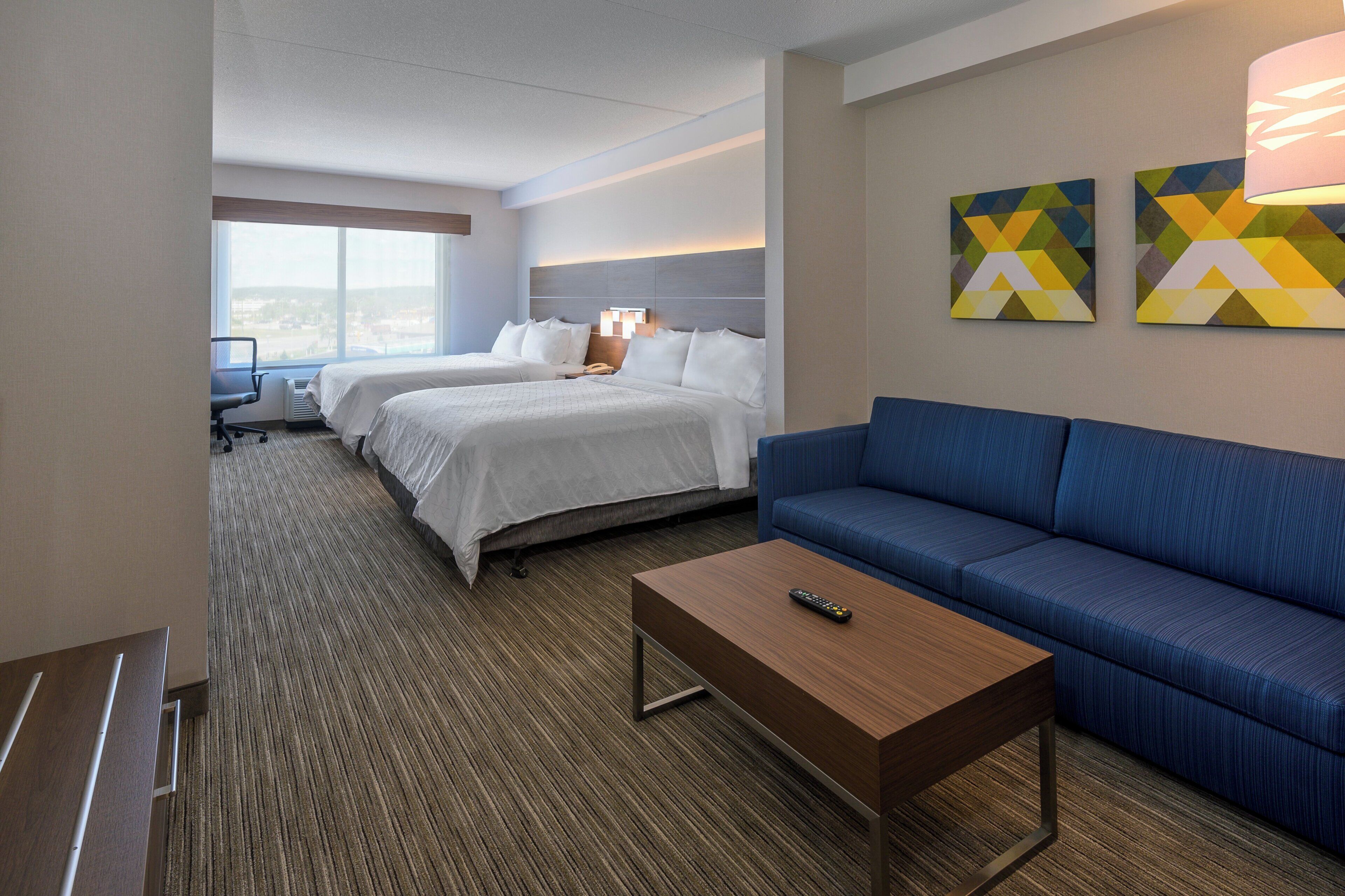 A hotel room with two beds, a blue sofa, a wooden coffee table, and a desk with a chair.