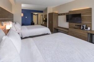 Habitación de hotel con dos camas, televisión, cafetera y escritorio.