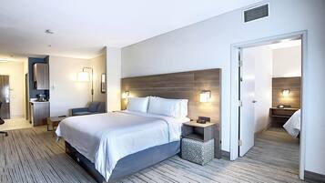 Une chambre d’hôtel moderne, dotée d’un grand lit, de tables de chevet, d’un bureau et d’une salle de bain visible à travers une porte ouverte.
