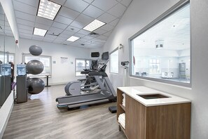 A fitness center with exercise equipment, a large window, and a wooden counter. - Holiday Inn Express Airport-Calgary by IHG (Calgary)