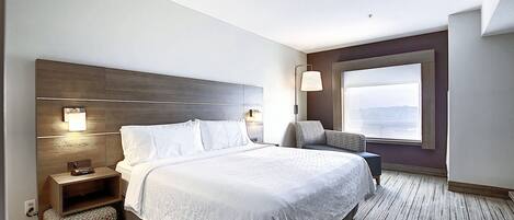 A hotel room with a large bed, a nightstand, a chair, a window with a view, and a wall-mounted lamp.