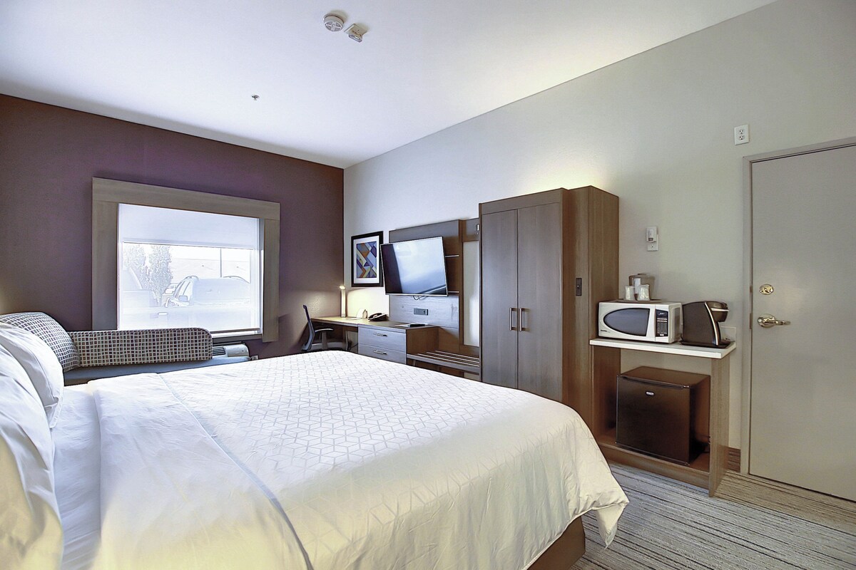 A hotel room with a bed, desk, television, microwave, and wardrobe.