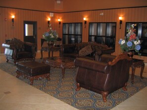 A lobby with a patterned carpet, leather armchairs, a coffee table, and wall-mounted lamps. - Holiday Inn Express Airport-Calgary by IHG (Calgary)