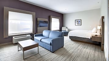 A hotel room with a large bed, a sofa, a TV, and a window.
