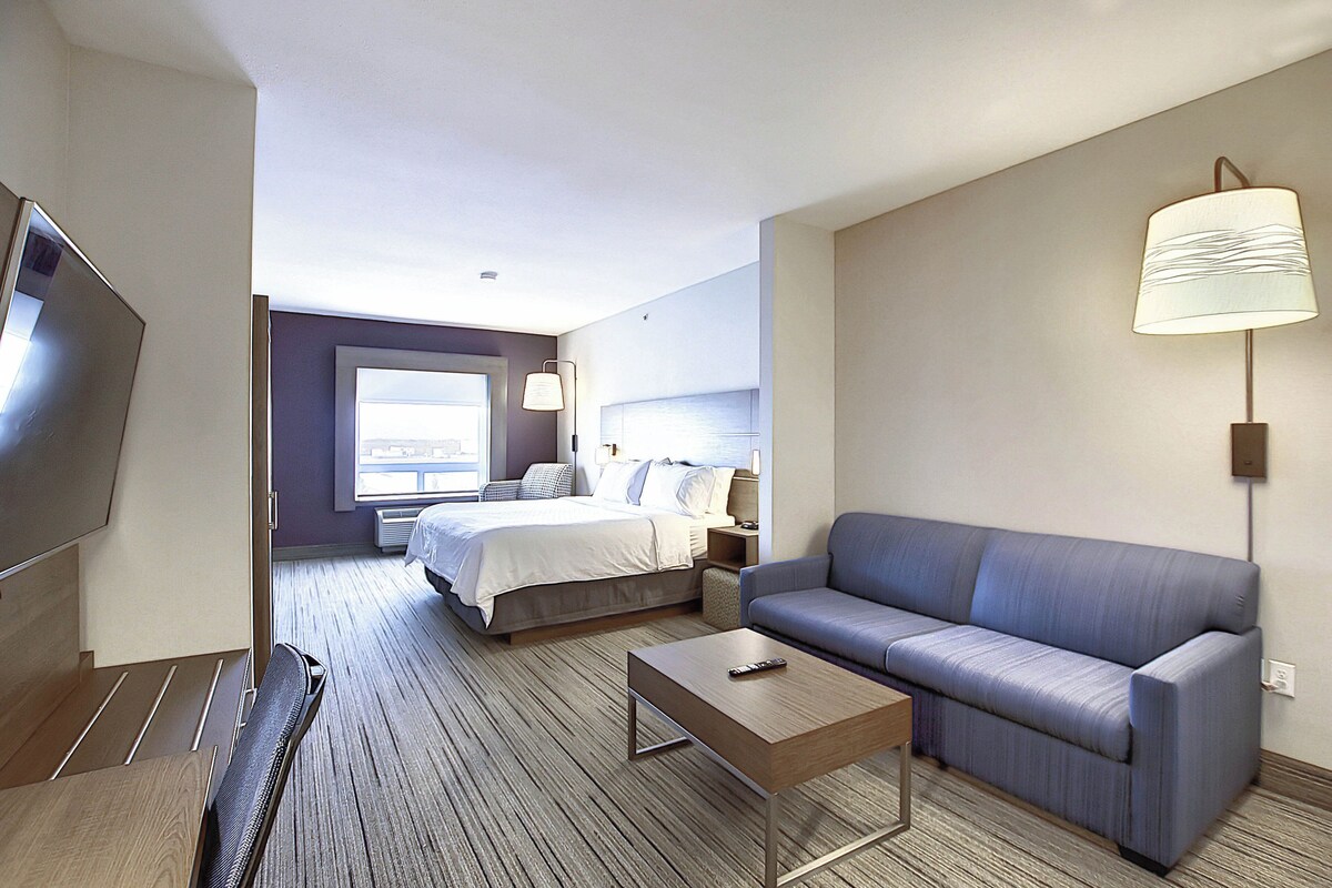 A hotel room with a bed, a sofa, a TV, a lamp, and a window.