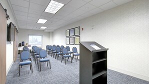 Un salón de conferencias con filas de sillas, un atril y cuadros en la pared.