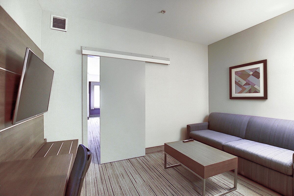 A modern hotel room with a sofa, a coffee table, a TV, and a door leading to a balcony.