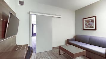 Une chambre d’hôtel moderne équipée d’un canapé, d’une table basse, d’une télévision et d’une porte donnant sur un balcon.