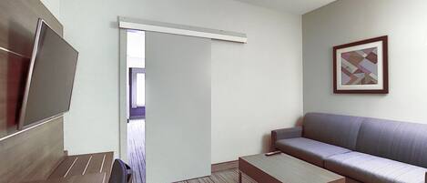 Une chambre d’hôtel moderne équipée d’un canapé, d’une table basse, d’une télévision et d’une porte donnant sur un balcon.