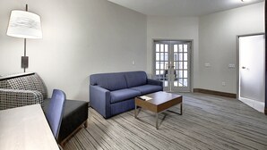 Habitación de hotel con un sofá azul, una mesita, una lámpara y una silla estampada.