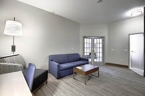 A hotel room with a blue sofa, a small table, a lamp, and a patterned chair. - Holiday Inn Express Airport-Calgary by IHG (Calgary)