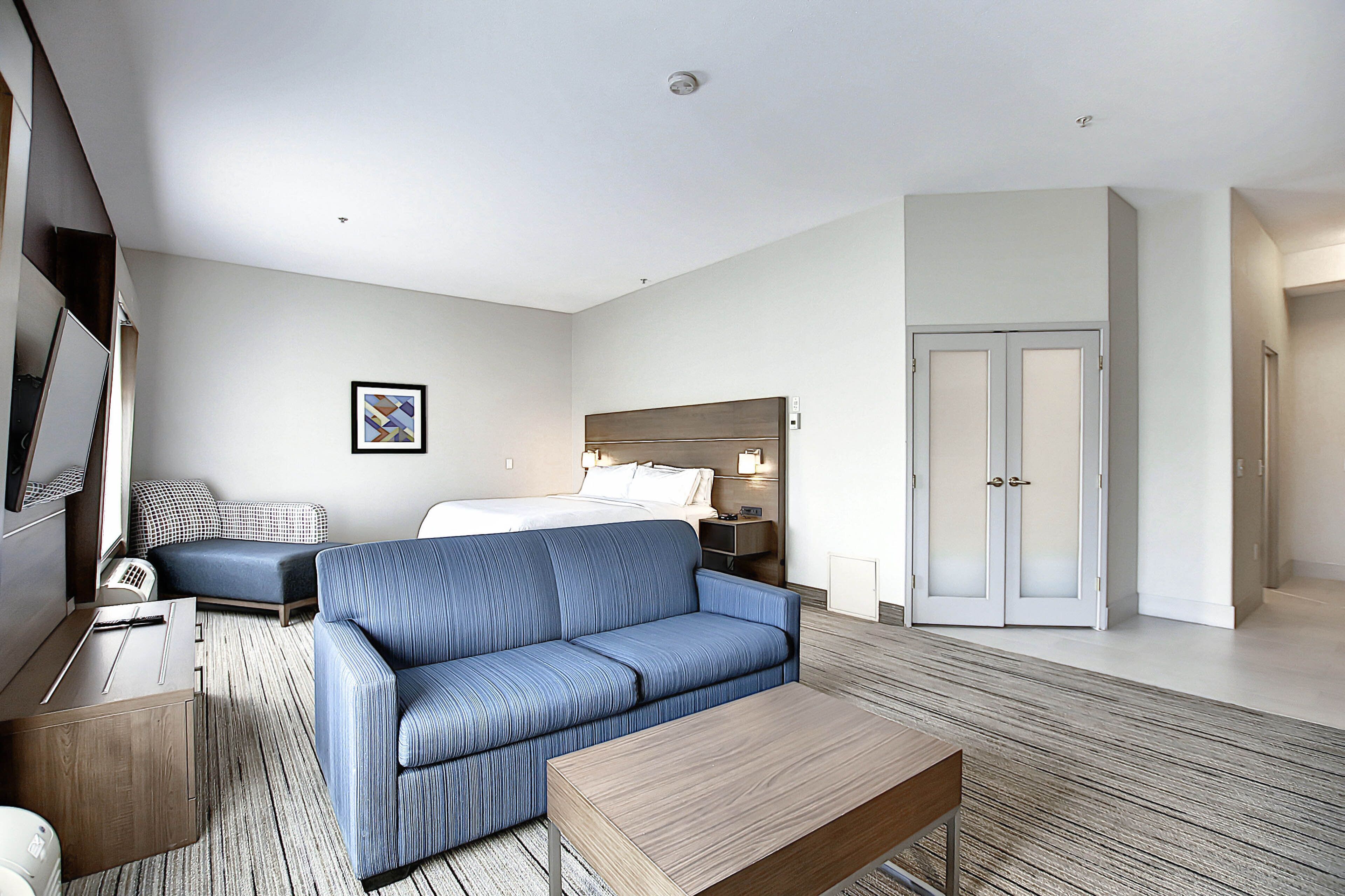 Ein modernes Hotelzimmer mit Bett, blauem Sofa, Holztisch, Schreibtisch mit Lampe und Kleiderschrank.