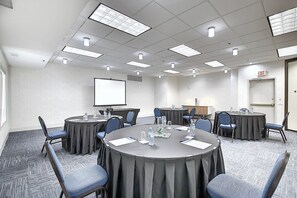 A conference room with round tables, chairs, a projector screen, and a water dispenser. - Holiday Inn Express Airport-Calgary by IHG (Calgary)