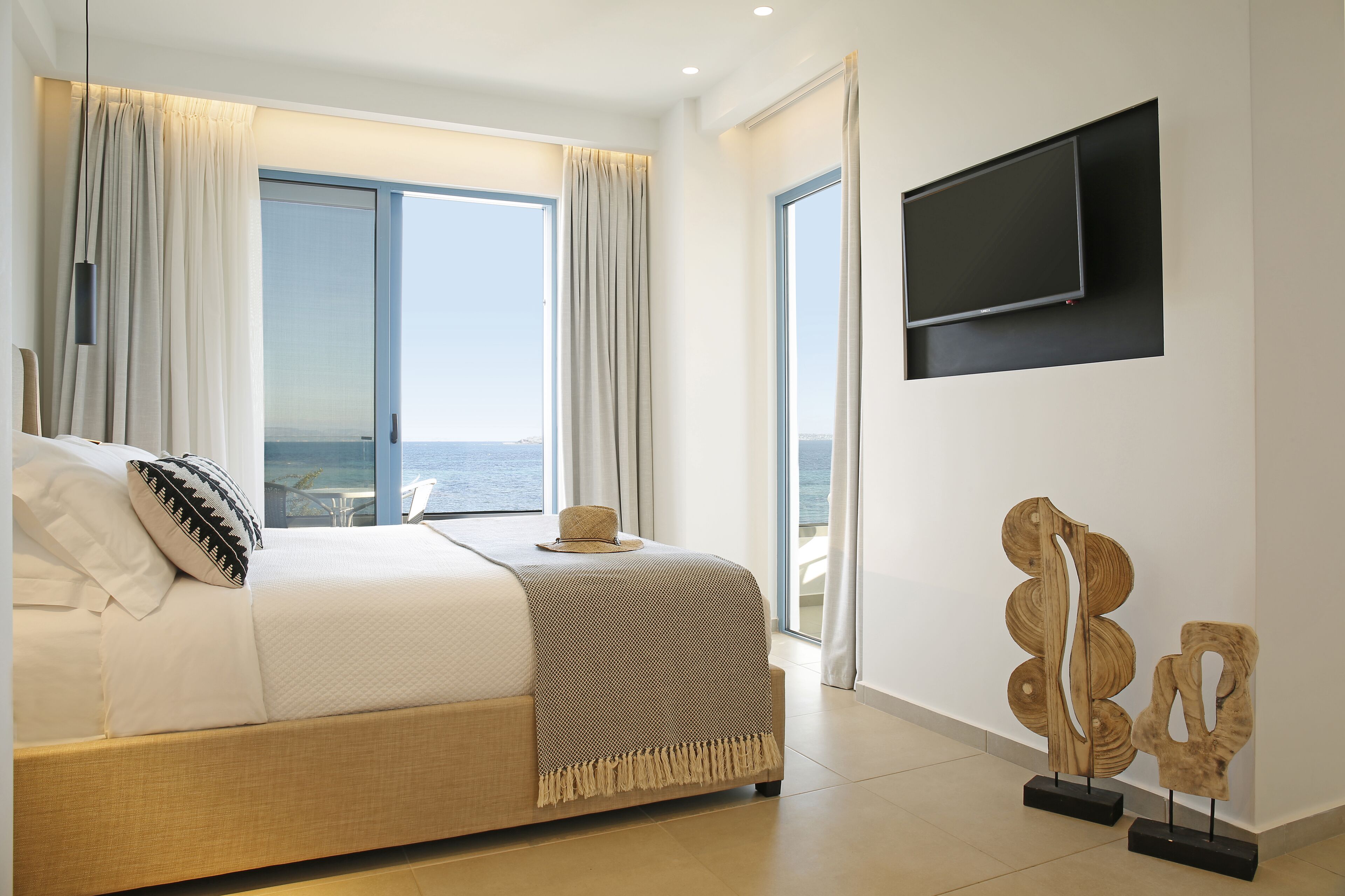 A hotel room with a bed, a view of the sea, a television, and a decorative wooden sculpture.