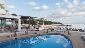 A pool area with lounge chairs and tables, a covered seating area, and a view of the sea. - Oasis Beach Hotel (Agistri)