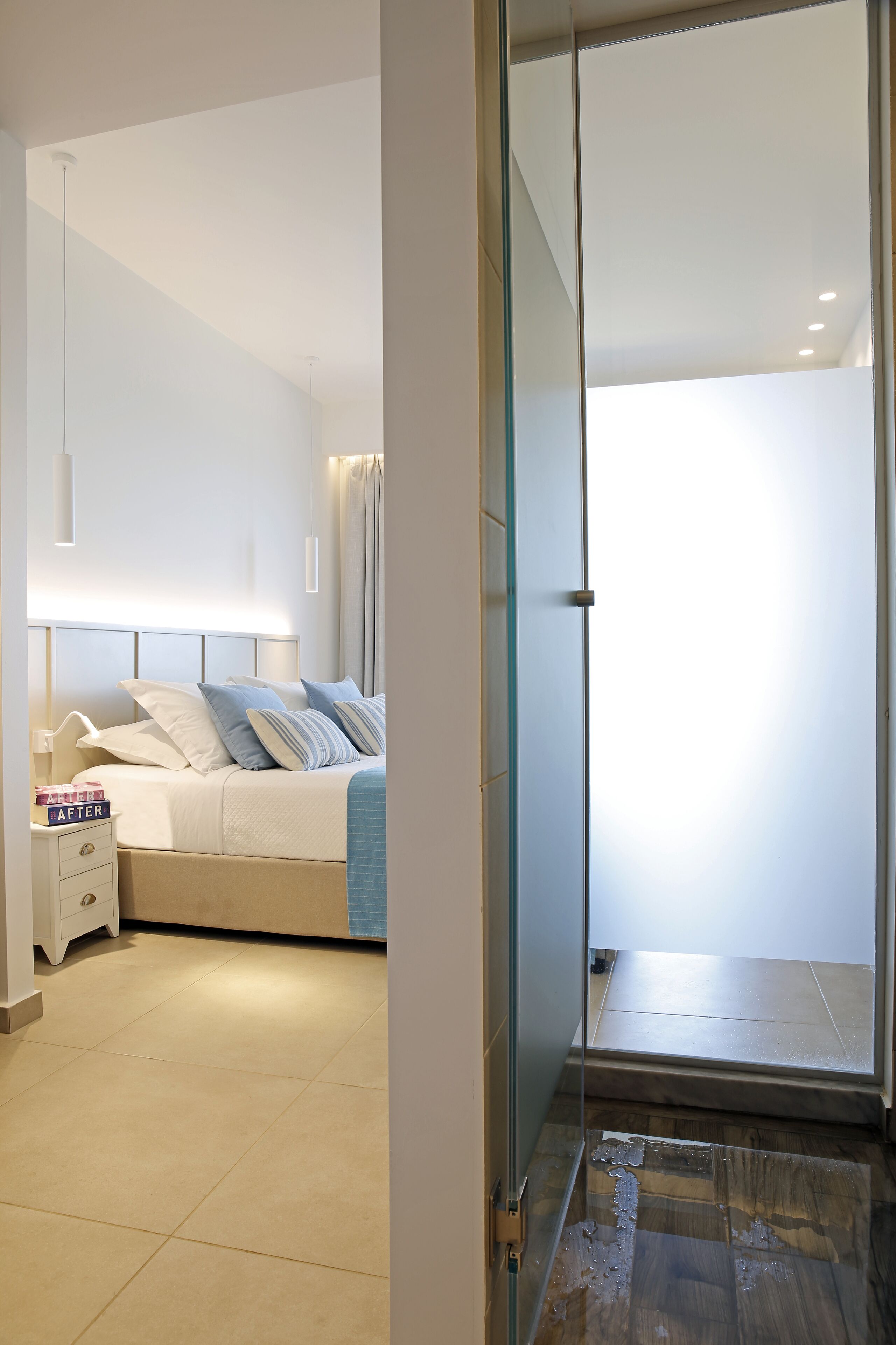 A modern bedroom with a bed, bedside tables, and a glass door leading to a bathroom.