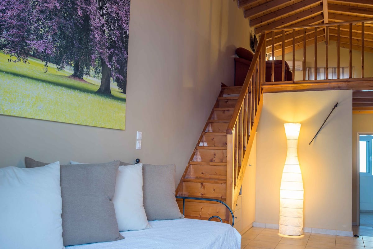 A room with a wooden staircase, a bed with pillows, and a large painting of trees.
