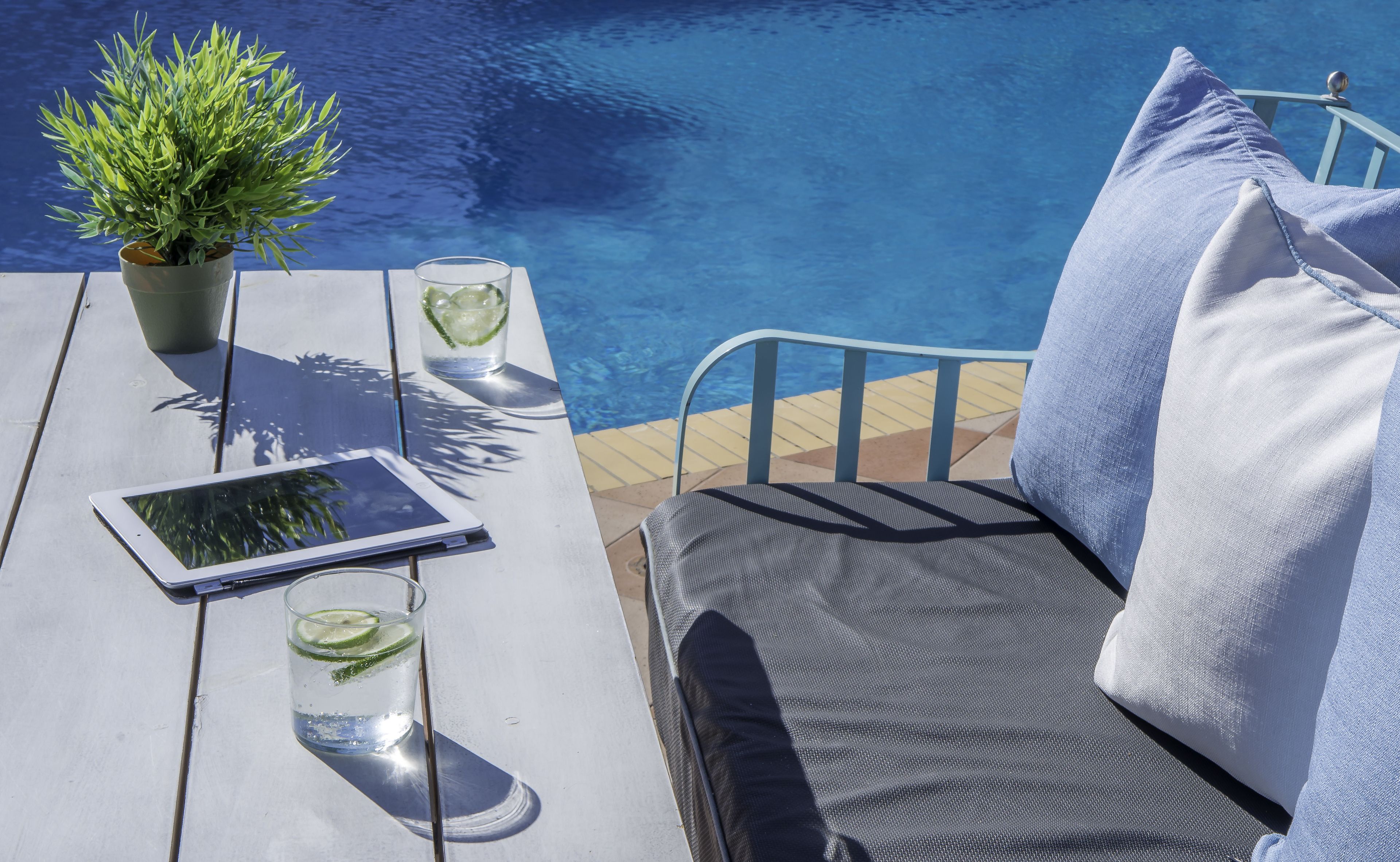 Ein Poolbereich mit Tisch, Tablet, zwei Gläsern mit Limettenscheiben und einem Blumentopf.