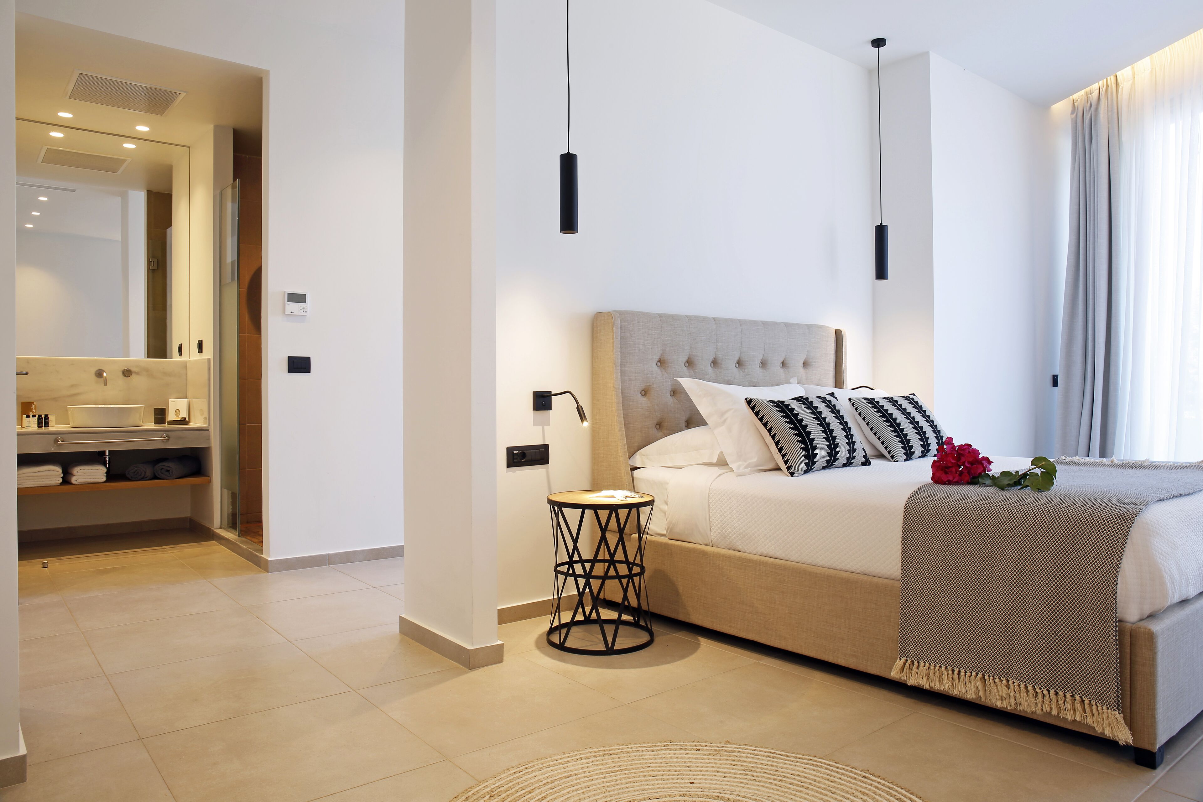 Una camera da letto moderna con un letto, un comodino e un bagno visibile attraverso una porta aperta.