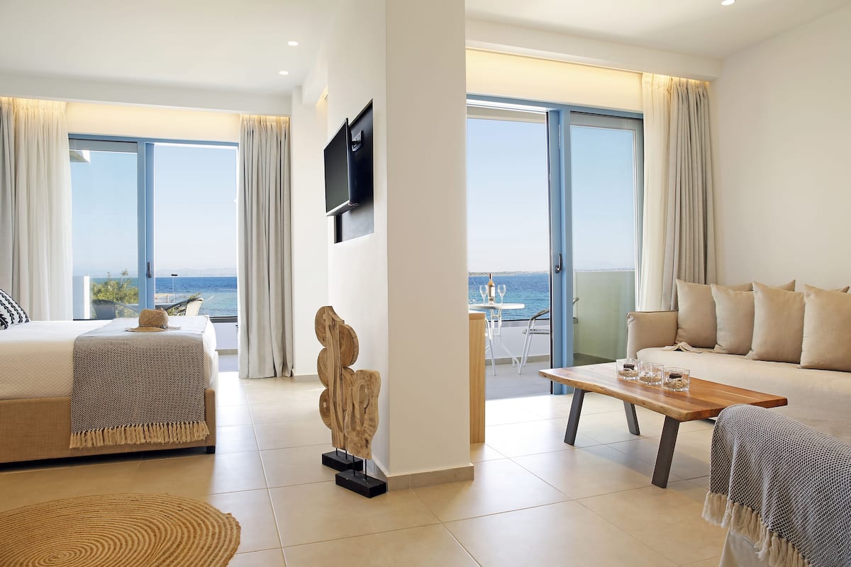 A modern hotel room with a bed, a sofa, a wooden coffee table, and a TV mounted on the wall.