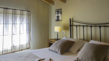 Una cama bien hecha con toallas enrolladas, techo de madera, ventana con persianas y una lámpara de noche.