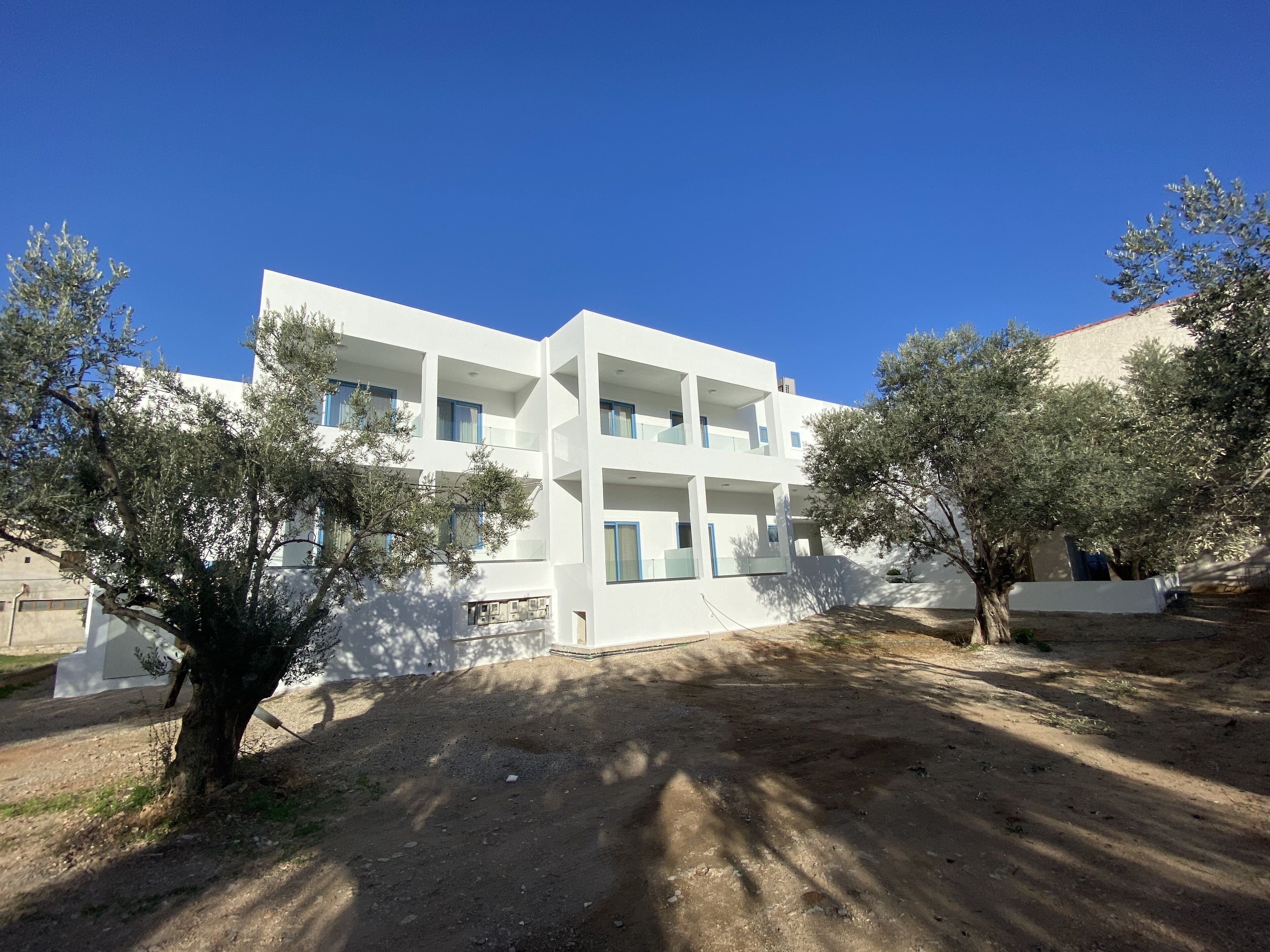 A modern white building with multiple balconies and a dirt ground area.