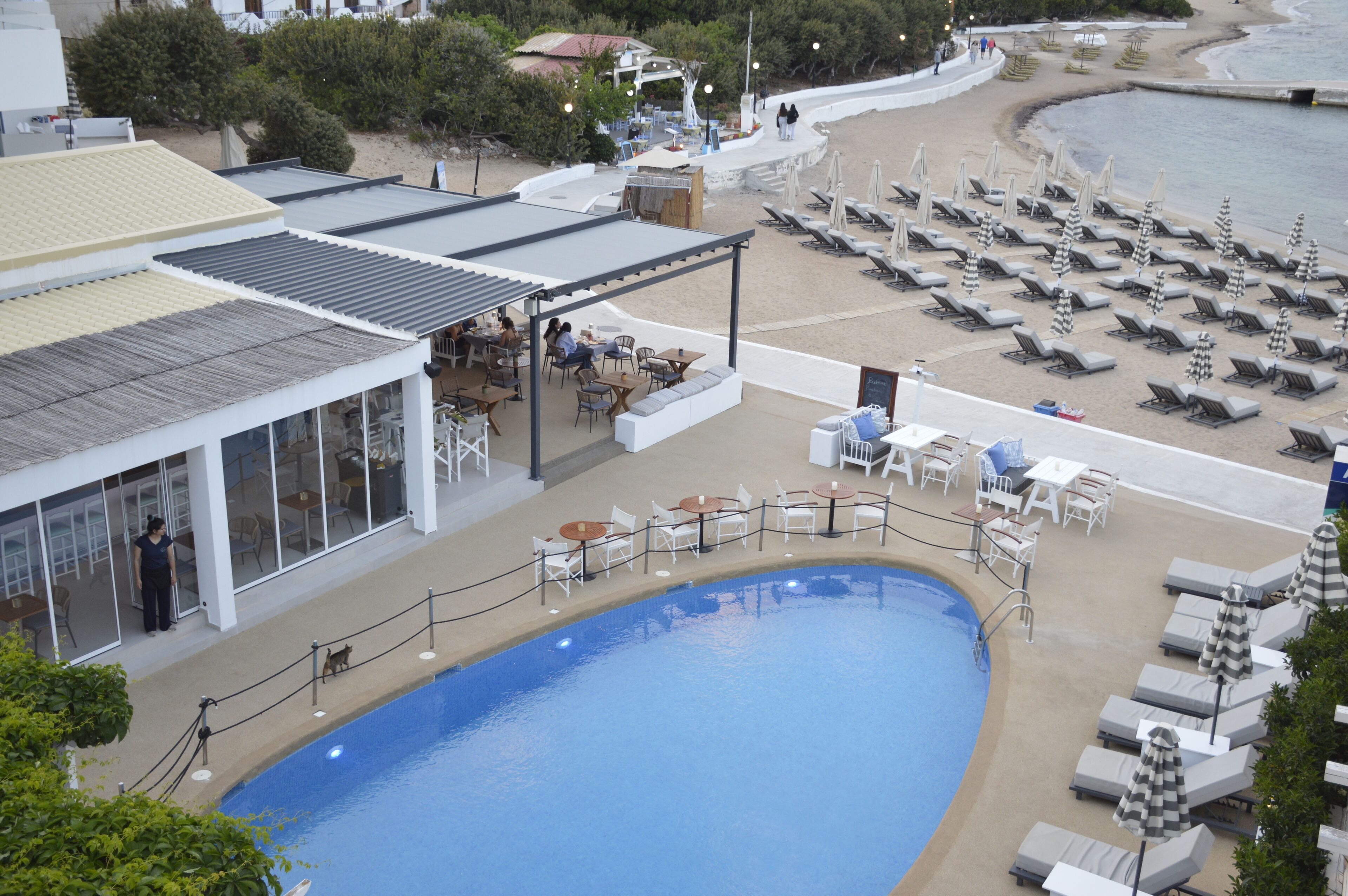 A poolside area with lounge chairs and tables, a covered seating area, and a view of the beach.