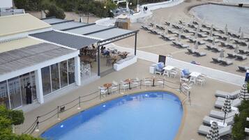 A poolside area with lounge chairs and tables, a covered seating area, and a view of the beach.