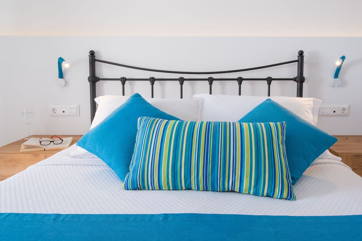 A bed with a black metal headboard, white bedding, and two pillows, one striped and one solid blue.