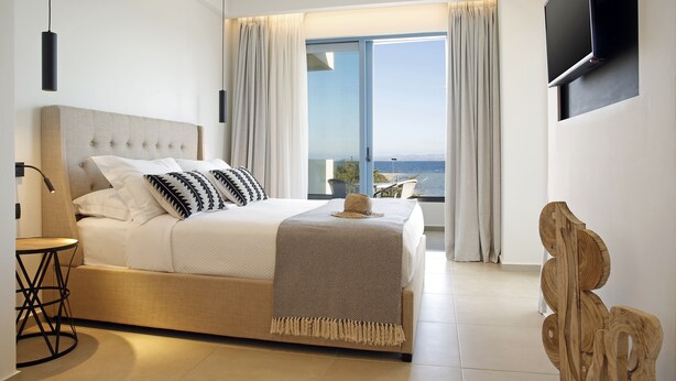 A modern bedroom with a large bed, a small table, and a TV mounted on the wall. - Oasis Beach Hotel (Agistri)