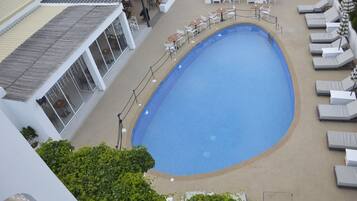 A swimming pool with lounge chairs and tables, surrounded by a fence.
