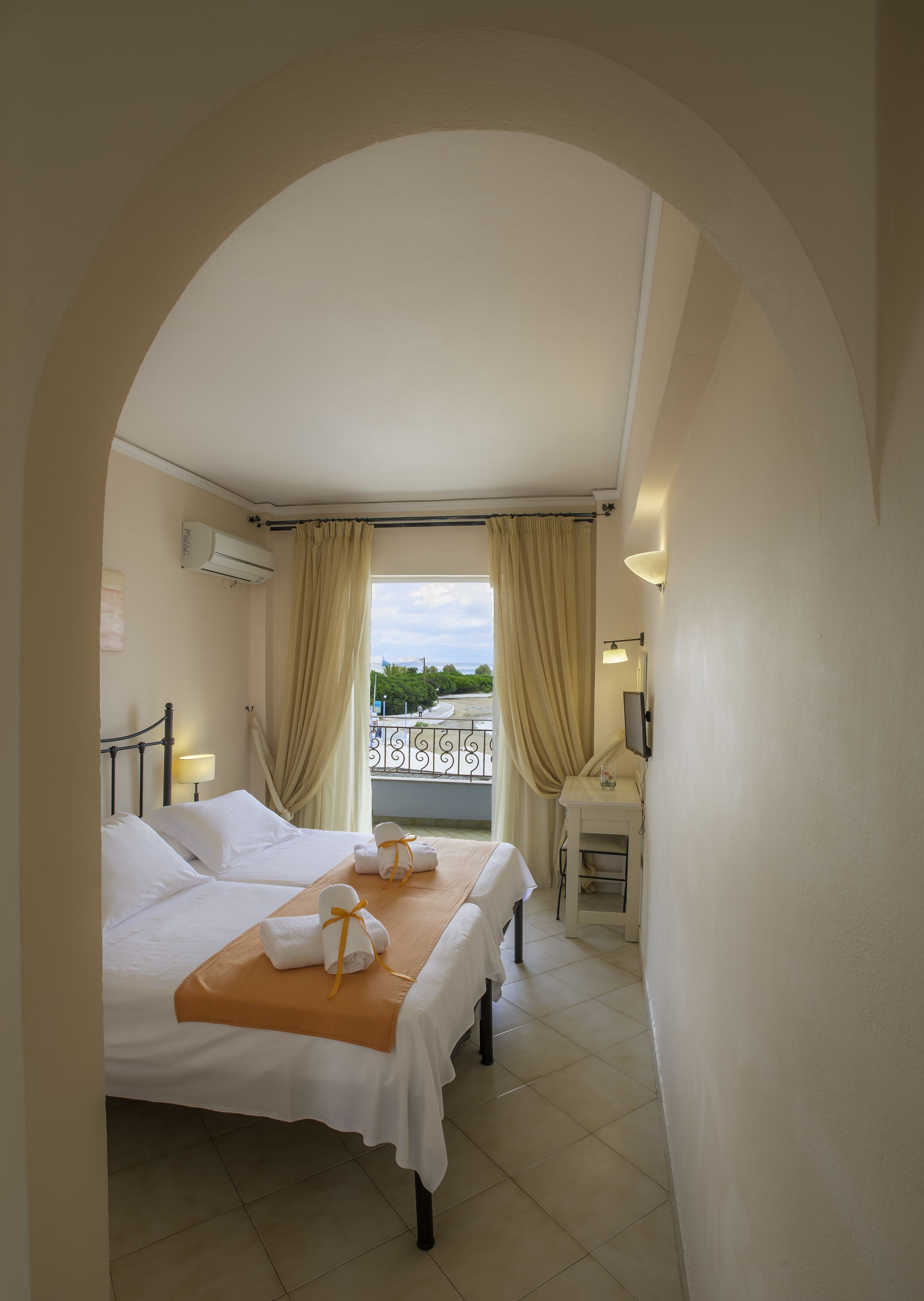 A hotel room with two beds, a balcony, a small table with towels, and a TV.