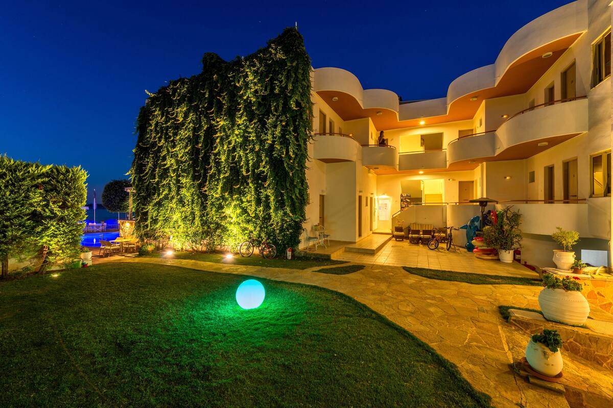 A hotel courtyard at night with a large illuminated sphere, a well-maintained lawn, and a building with balconies and potted plants.
