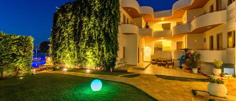 A hotel courtyard at night with a large illuminated sphere, a well-maintained lawn, and a building with balconies and potted plants.